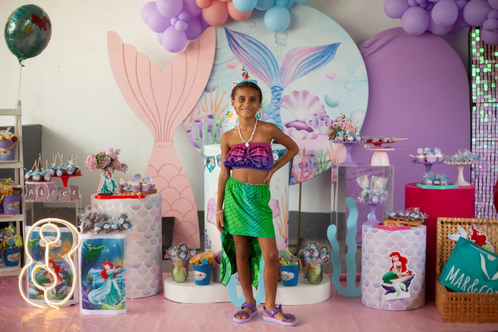 Menina com vestido de sereia junto à mesa decorada da festa